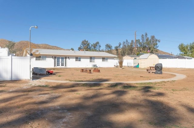 rear view of property with an outbuilding, french doors, a fenced backyard, and a shed