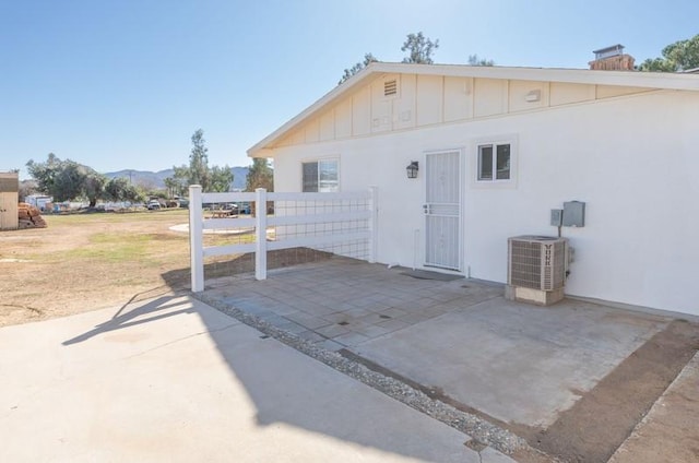 rear view of property with cooling unit, a mountain view, fence, board and batten siding, and a patio area