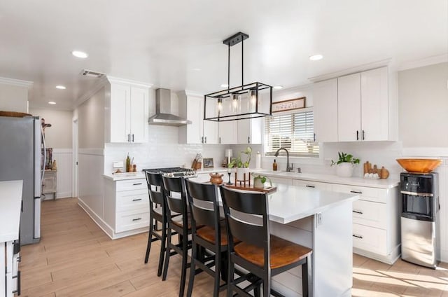 kitchen with wall chimney exhaust hood, ornamental molding, freestanding refrigerator, light countertops, and white cabinetry