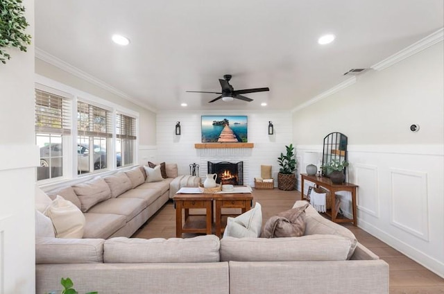 living room with a warm lit fireplace, visible vents, ornamental molding, and light wood-style flooring