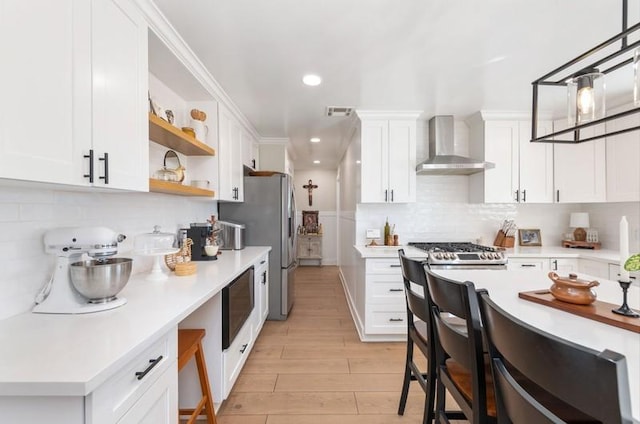 kitchen featuring white cabinets, light countertops, wall chimney range hood, backsplash, and open shelves