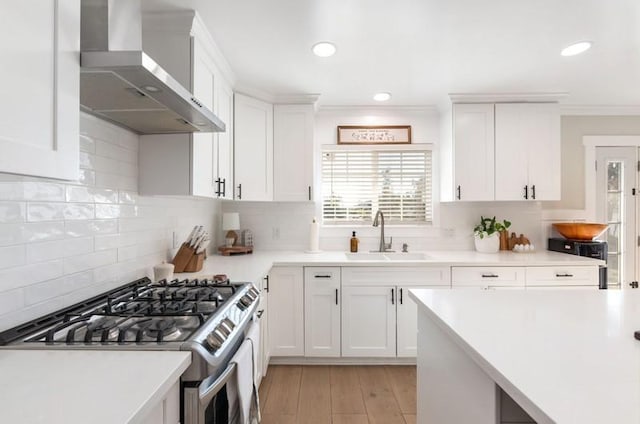 kitchen featuring light countertops, gas stove, white cabinetry, a sink, and wall chimney exhaust hood