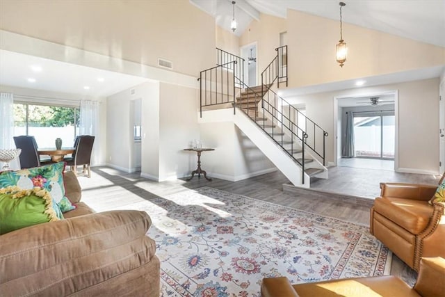 living area featuring baseboards, wood finished floors, stairs, high vaulted ceiling, and beam ceiling