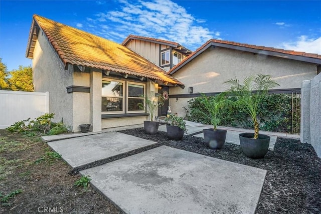 rear view of property featuring a patio area, fence, a tile roof, and stucco siding