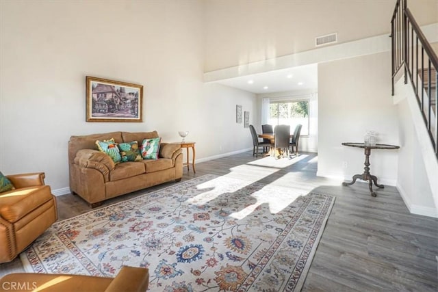 living room with baseboards, visible vents, dark wood finished floors, a towering ceiling, and stairs