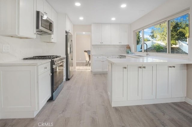 kitchen with light wood finished floors, light countertops, appliances with stainless steel finishes, white cabinetry, and a sink