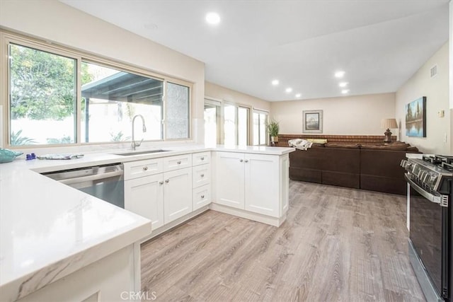 kitchen featuring a sink, white cabinetry, open floor plan, light countertops, and appliances with stainless steel finishes