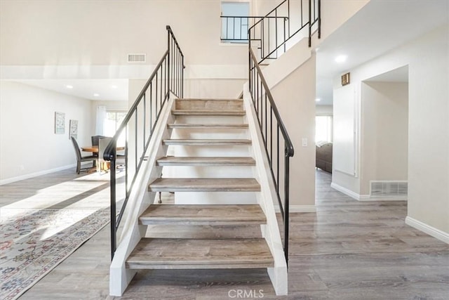 staircase with baseboards, visible vents, a high ceiling, and wood finished floors