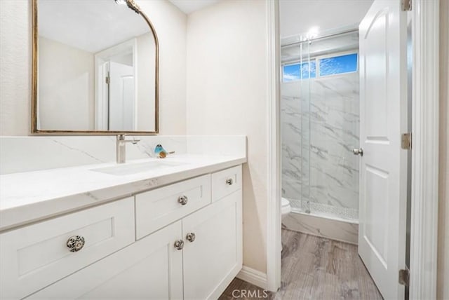 bathroom featuring toilet, wood finished floors, a marble finish shower, and vanity