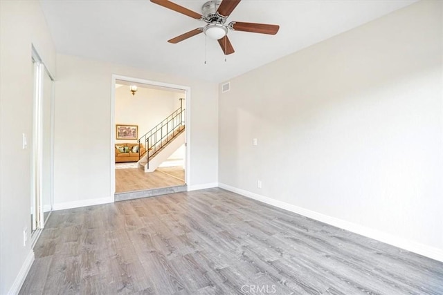 empty room with light wood finished floors, visible vents, stairway, ceiling fan, and baseboards