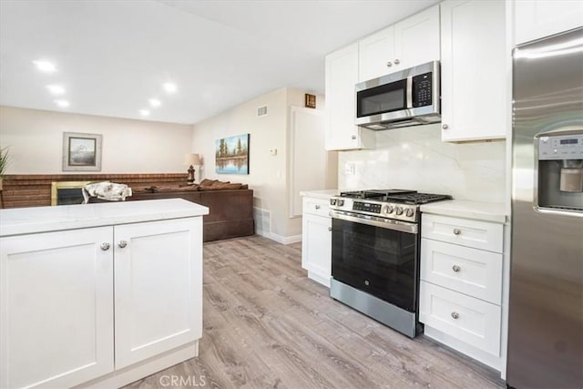 kitchen with open floor plan, stainless steel appliances, light countertops, and white cabinetry