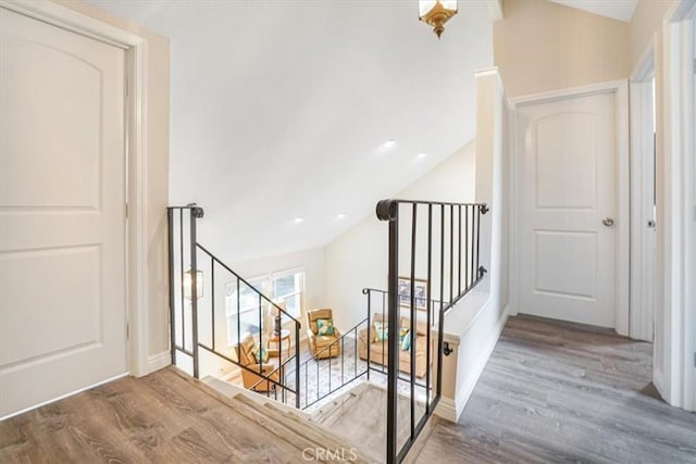 corridor with baseboards, vaulted ceiling, wood finished floors, and an upstairs landing