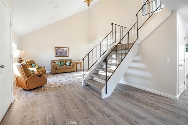 staircase featuring high vaulted ceiling, wood finished floors, and baseboards