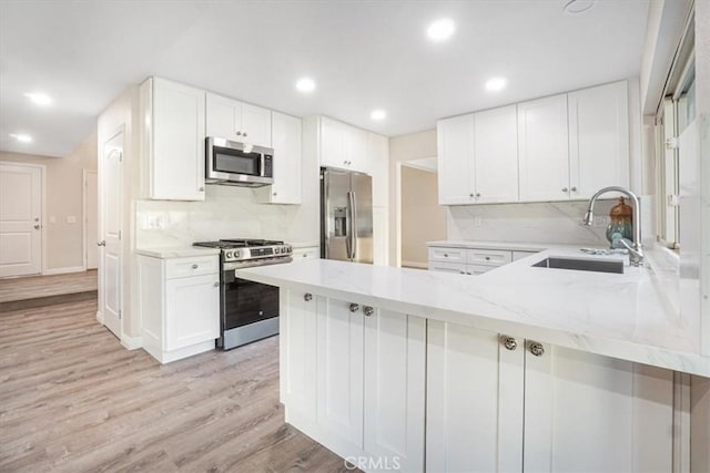 kitchen with light stone counters, a peninsula, a sink, white cabinets, and appliances with stainless steel finishes