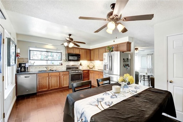 kitchen with stainless steel appliances, backsplash, brown cabinetry, a sink, and a textured ceiling