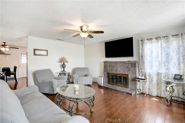 living room featuring visible vents, a glass covered fireplace, ceiling fan, wood finished floors, and a textured ceiling