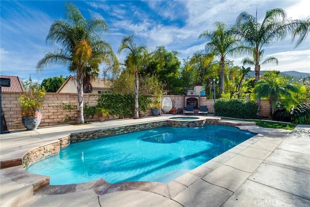 view of swimming pool with a pool with connected hot tub, a patio area, a fenced backyard, and an outdoor fireplace