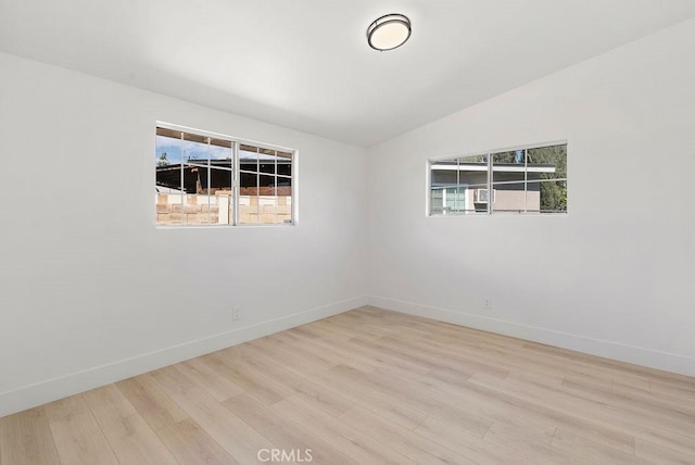 empty room with light wood-type flooring, baseboards, and vaulted ceiling