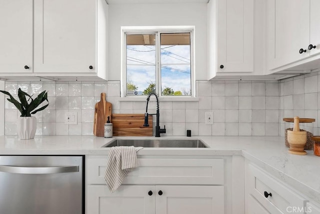 kitchen featuring stainless steel dishwasher, a sink, light stone counters, and white cabinets