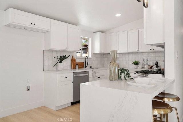 kitchen with lofted ceiling, appliances with stainless steel finishes, light countertops, a kitchen bar, and white cabinetry