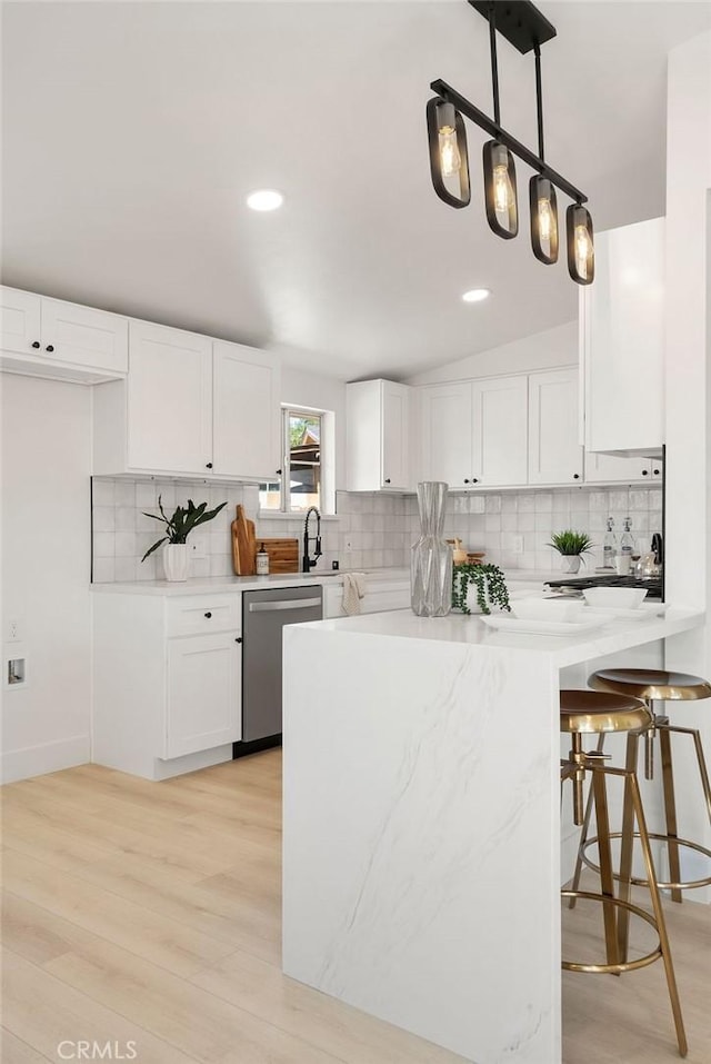 kitchen with white cabinets, light wood-style flooring, hanging light fixtures, light countertops, and stainless steel dishwasher