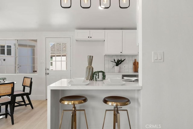 kitchen with white cabinets, decorative backsplash, a breakfast bar, light countertops, and light wood-style floors