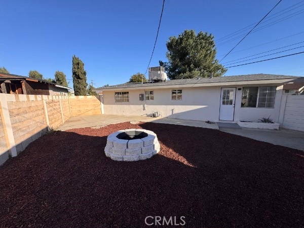 rear view of property with a patio, an outdoor fire pit, central AC unit, a fenced backyard, and stucco siding