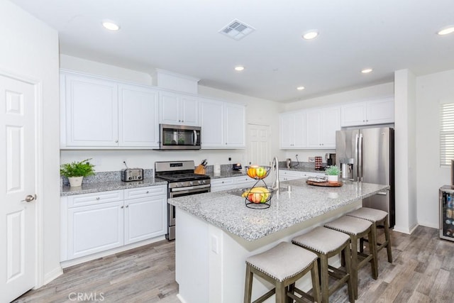 kitchen featuring appliances with stainless steel finishes, white cabinets, visible vents, and a breakfast bar area