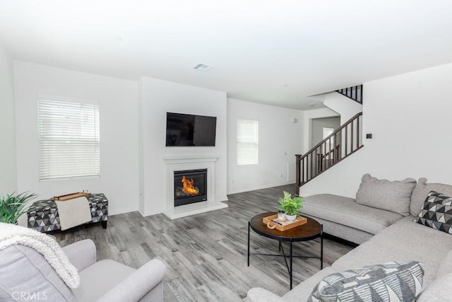 living area featuring stairs, a glass covered fireplace, wood finished floors, and visible vents