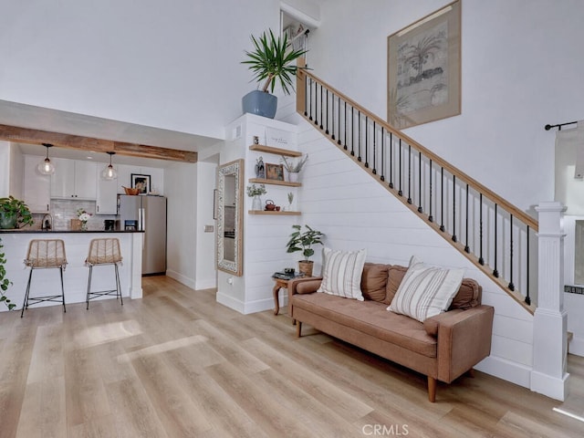 living area featuring a high ceiling, stairway, light wood-style flooring, and baseboards