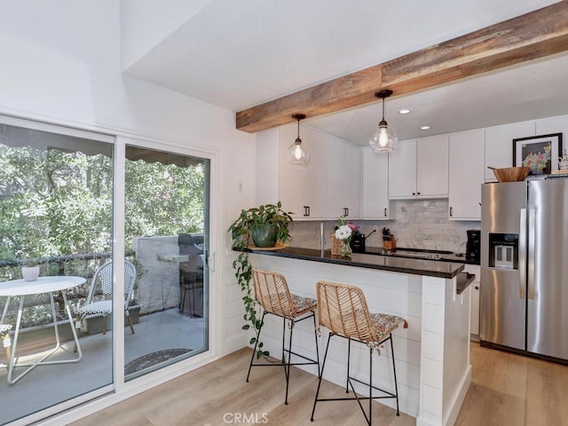 kitchen featuring stainless steel fridge, white cabinets, a kitchen breakfast bar, hanging light fixtures, and a peninsula