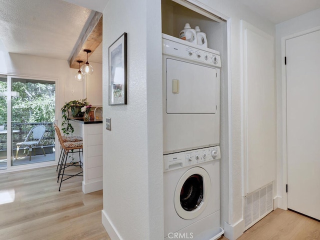 clothes washing area featuring light wood finished floors, stacked washer and dryer, visible vents, laundry area, and baseboards