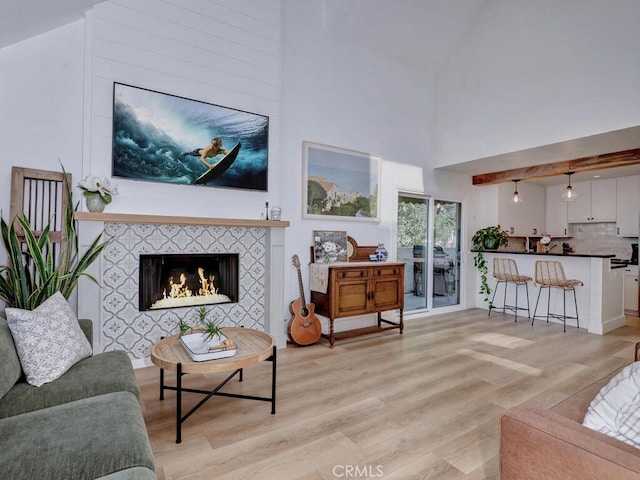 living area featuring light wood-style floors, a high ceiling, and a tile fireplace