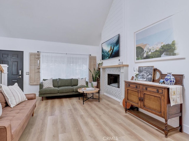 living area with high vaulted ceiling, a tile fireplace, light wood-style flooring, and baseboards