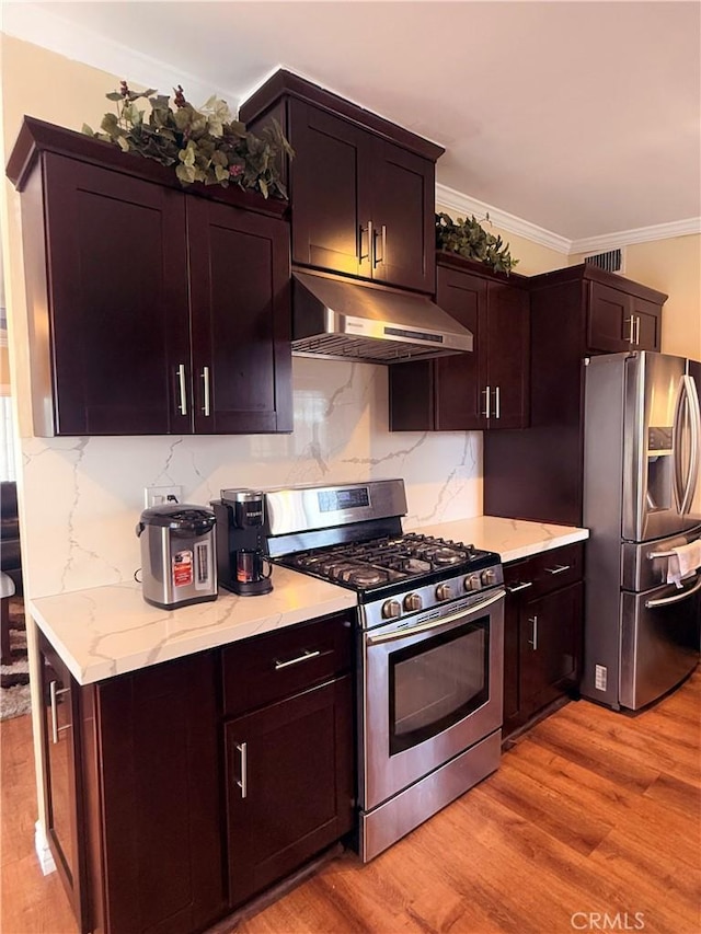 kitchen with under cabinet range hood, appliances with stainless steel finishes, light wood-type flooring, decorative backsplash, and crown molding