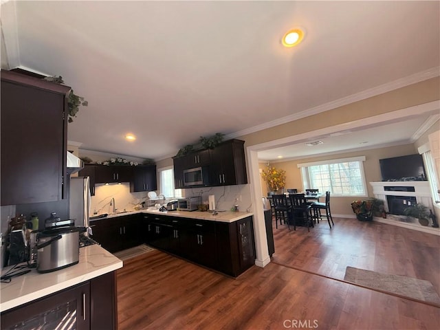 kitchen with baseboards, a glass covered fireplace, stainless steel microwave, ornamental molding, and dark wood-type flooring