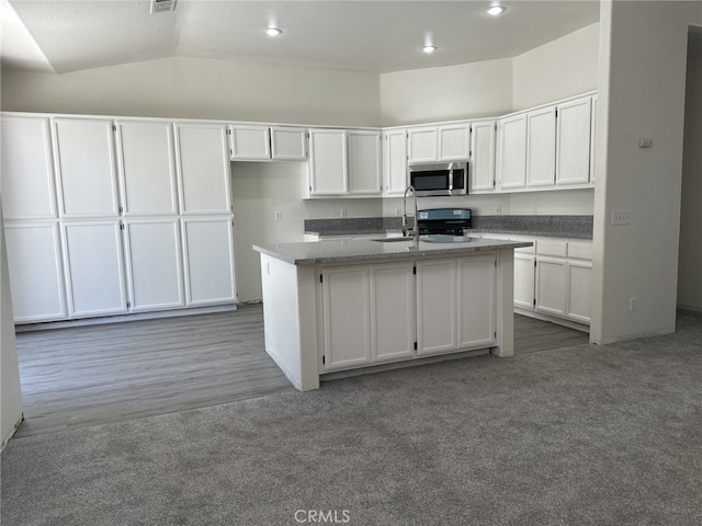 kitchen featuring a kitchen island with sink, stainless steel microwave, white cabinets, and dark colored carpet