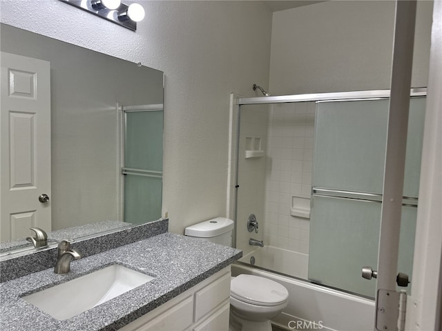 bathroom featuring toilet, a textured wall, enclosed tub / shower combo, and vanity