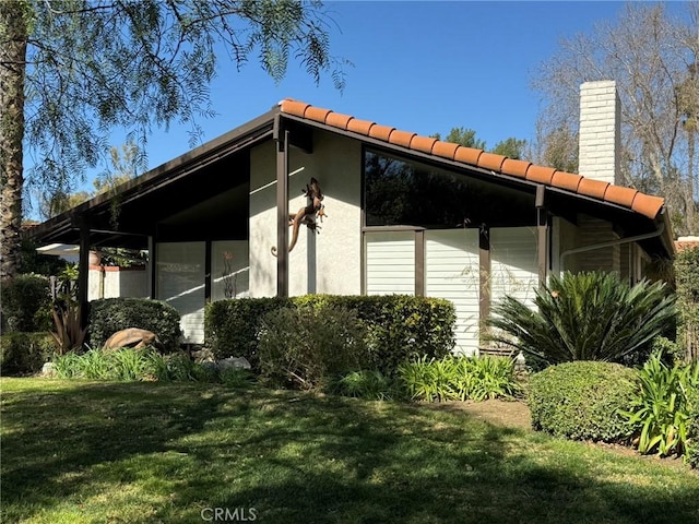 view of side of property with a chimney, a lawn, and a tiled roof