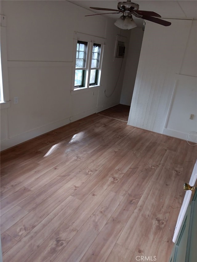 empty room featuring ceiling fan, an AC wall unit, light wood-type flooring, and baseboards