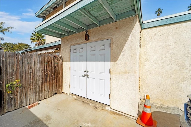 view of exterior entry featuring fence, a patio, and stucco siding