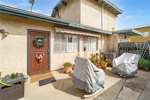 doorway to property featuring central air condition unit, fence, a patio, and stucco siding