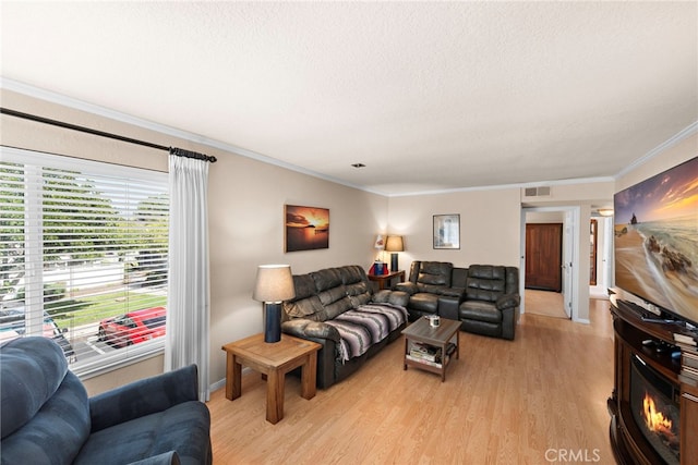 living room with ornamental molding, light wood-style flooring, a textured ceiling, and visible vents