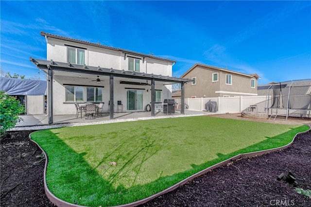 back of house with a patio, a fenced backyard, a yard, stucco siding, and a trampoline