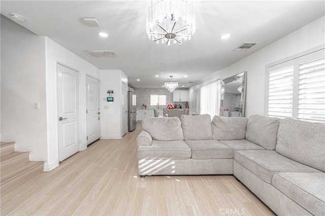 living room with visible vents, light wood-style flooring, and an inviting chandelier