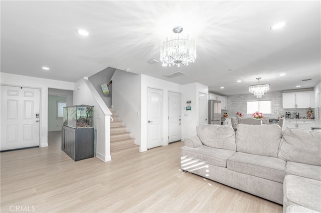 living room with recessed lighting, visible vents, light wood-style flooring, an inviting chandelier, and stairs