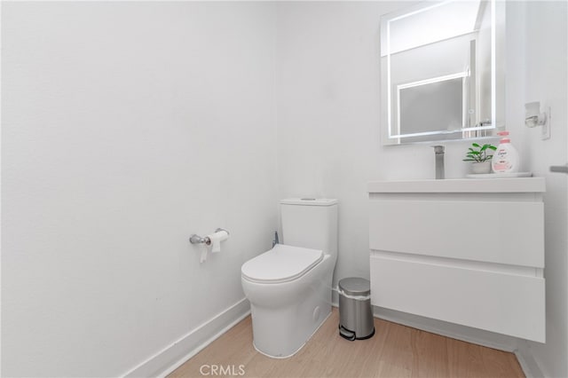 half bathroom with wood finished floors, toilet, and baseboards