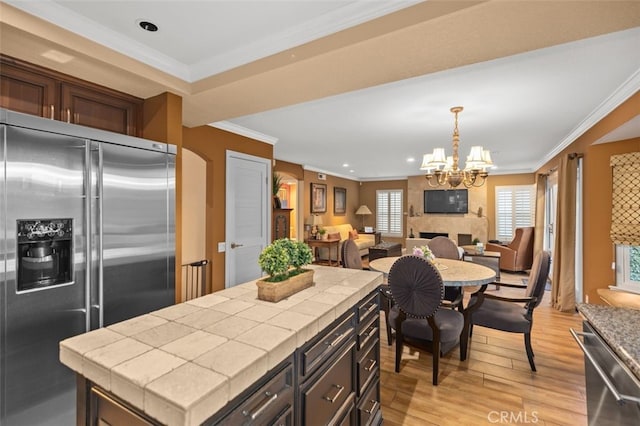 kitchen featuring pendant lighting, crown molding, stainless steel appliances, open floor plan, and dark brown cabinetry