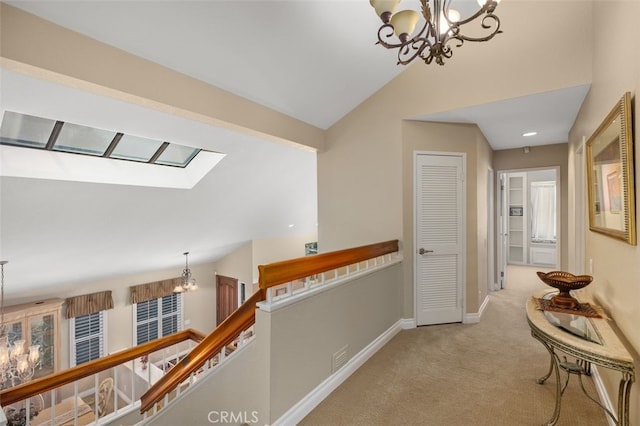 corridor featuring vaulted ceiling with skylight, light colored carpet, a notable chandelier, an upstairs landing, and baseboards