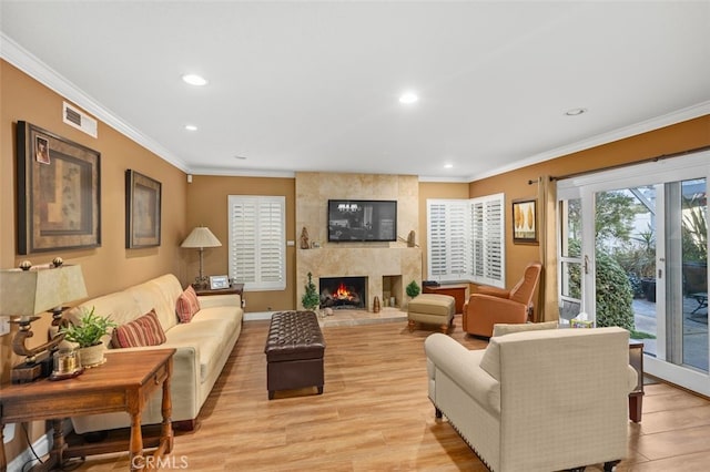 living room featuring a large fireplace, light wood-type flooring, visible vents, and crown molding